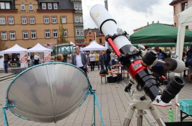 Ein Teleskop steht in der Innenstadt. Im unscharfen Hintergrund sind viele Menschen.