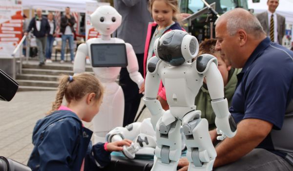 Im Vordergrund steht ein weißer Roboter. Dahinter stehen Kinder und der Bürgermeister Dr. Heiko Voigt.