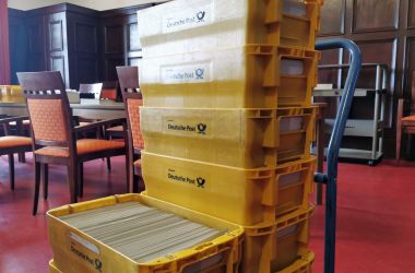 Mehrere gelbe Kisten mit der Aufschrift Deutsche Post sind aufeinander gestapelt. Sie sind mit Briefen gefüllt.