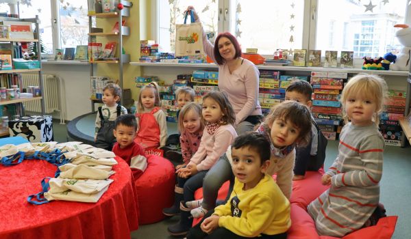 Kleine Kinder und eine Frau sitzen auf Sitzkissen in der Bibliothek.