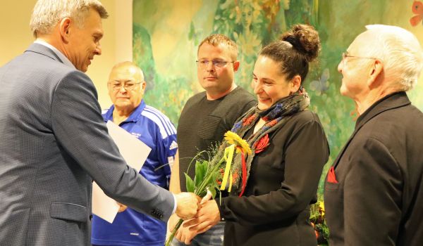Der Bürgermeister Dr. Heiko Voigt überreicht eine Urkunde und Blumen an einen Mann und eine Frau.