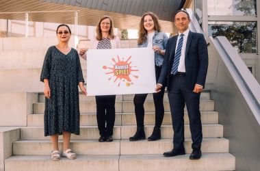 Vier Personen halten ein Plakat mit der Aufschrift Kunstspiel.