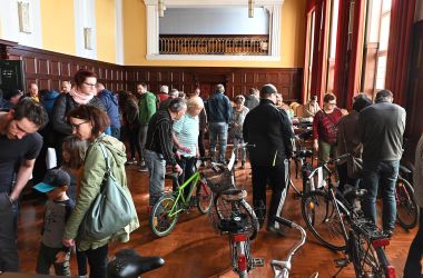 Viele Menschen stehen in einem Saal und schauen sich Fahrräder an.