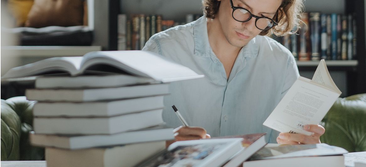 Ein Mann sitzt an einem Tisch. Auf dem Tisch liegt ein Stapel Bücher.