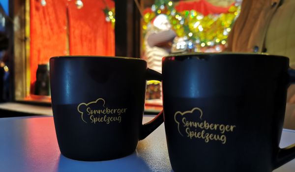 Auf einem Tisch stehen zwei schwarze Tassen mit der Aufschrift: Sonneberger Spielzeug.