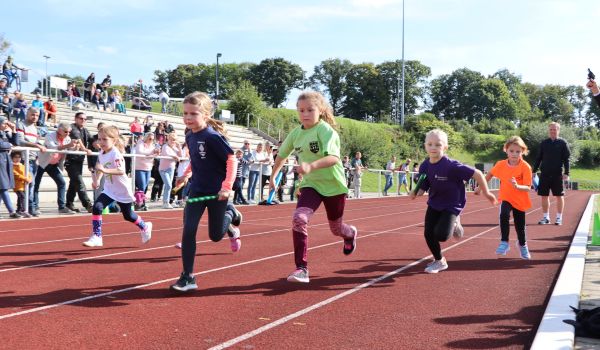 Kinder in Sportbekleidung rennen über eine Laufbahn in einem Station.