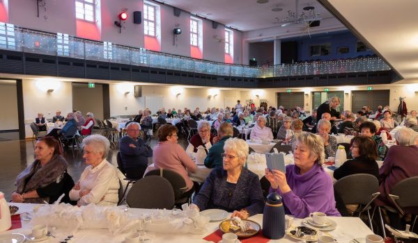 Viele Senioren sitzen an gedeckten Kaffeetafeln in einem großen Saal.