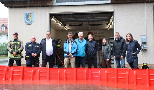 Eine mobile Barriere für Hochwasserschutz wird vor einem Gebäude getestet. Dahinter steht eine Reihe von Personen.