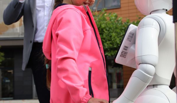 Ein Mädchen steht neben einem weißen Roboter. Dahinter steht der Bürgermeister.