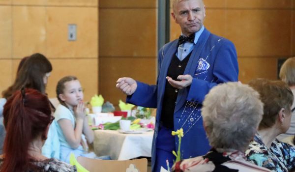 Ein Zauberer in blauem Anzug steht zwischen sitzenden Menschen.