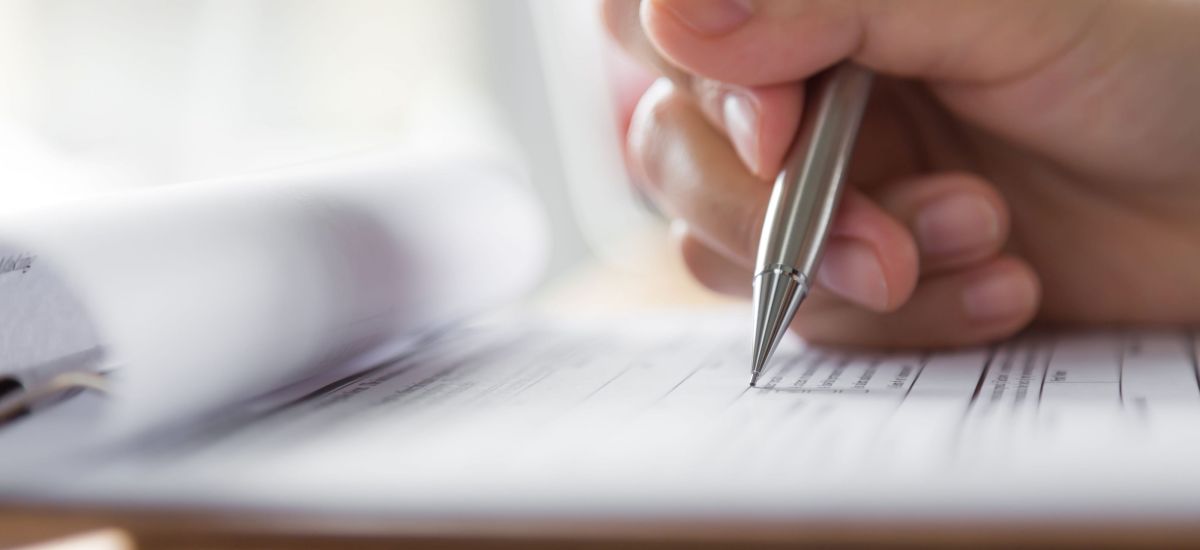 Eine Hand schreibt mit einem Stift auf ein Formular.