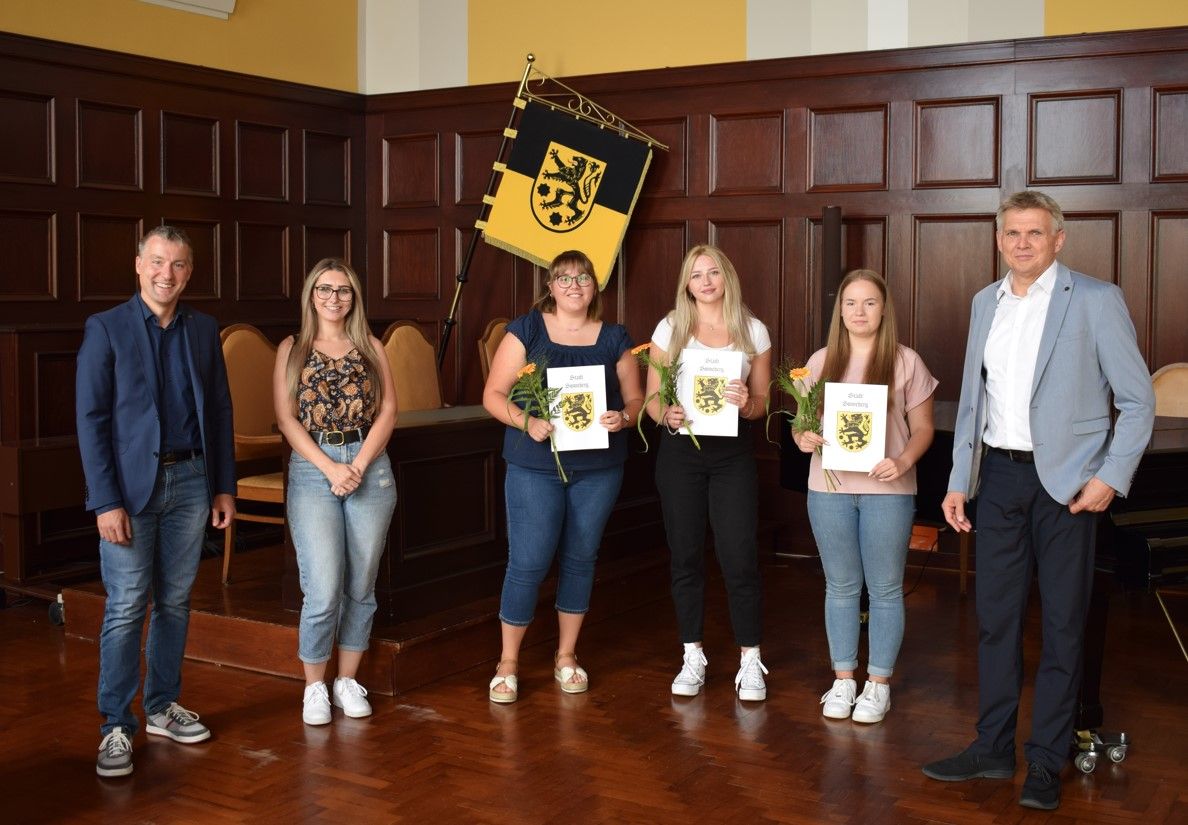 Sechs Personen stehen in einer Reihe nebeneinander. Davon halten drei junge Frauen eine Mappe und eine Blume in den Händen. Es sind die neuen Auszubildenden der Stadt Sonneberg.