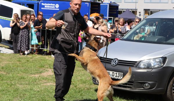 Ein Mann hält eine Tütchen mit Drogen in der einen und einen Spürhund in der anderen Hand.