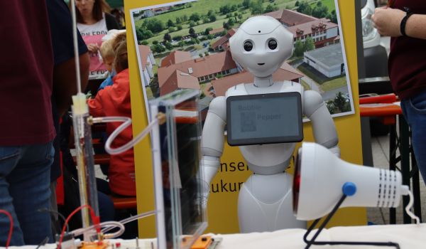 Auf einem Tisch sind Experimente aufgebaut. Dahinter steht ein weißer Roboter.