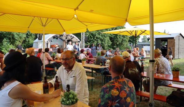 Menschen sitzen auf Bierzeltgarnituren unter Sonnenschirmen.