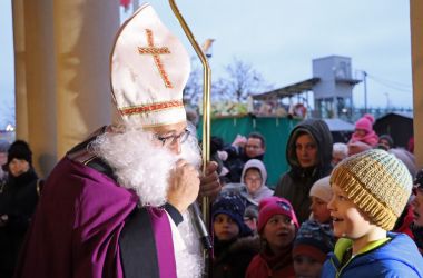 Ein Mann in Nikolaus-Kostüm mit goldenem Zepter. Um ihn herum stehen viele Kinder.