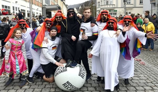 Mehrere Personen sind als Scheichs gekleidet. Davor liegt ein Fußball mit der Aufschrift: Menschenrechte.