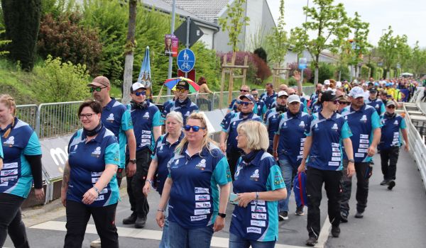 Viele Menschen in blauen Trikots laufen einer Straße entlang.