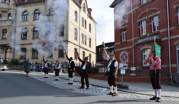Männer in Tracht stehen in der Stadt und schießen mit alten Pistolen in die Luft. Es ist ein Schützenverein.