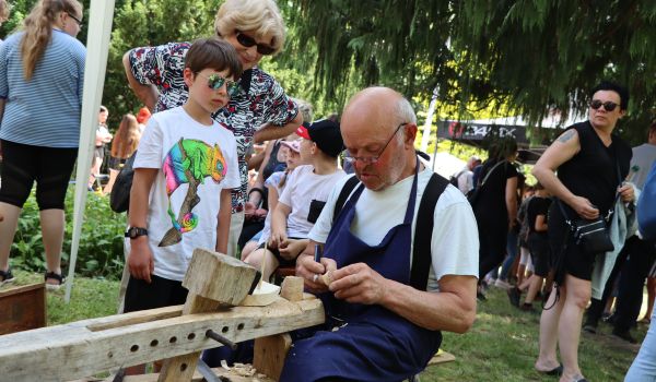 Ein Schnitzer macht mit einem Jungen ein Schiff aus Holz.