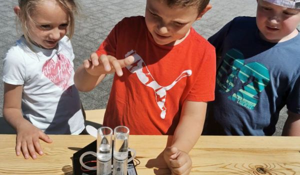 Drei Kinder stehen an einem Tisch. Auf dem Tisch steht eine Brennstoffzelle zum Experimentieren mit Wasserstoff.