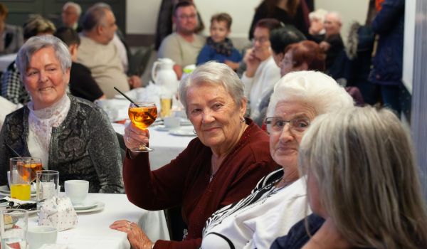 Senioren sitzen an gedeckten Kaffeetafeln in einem großen Saal.