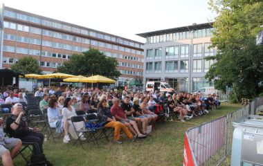 Viele Menschen sitzen in Stuhlreihen vor einer Bühne.