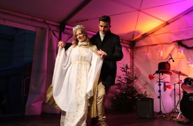 Eine Frau als Christkind gekleidet tanzt mit einem Mann auf einer Bühne.