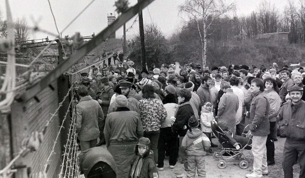 Schwarz-weiß: Viele Menschen stehen vor einem Grenzzaun.