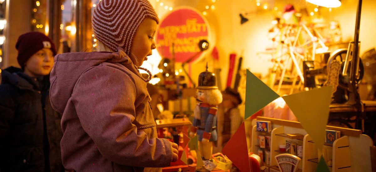 Kinder schauen in ein weihnachtlich geschmücktes Schaufenster.