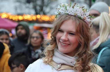 Ein blondes Mädchen hat ein Christkind-Kostüm an und läuft über einen Weihnachtsmarkt.