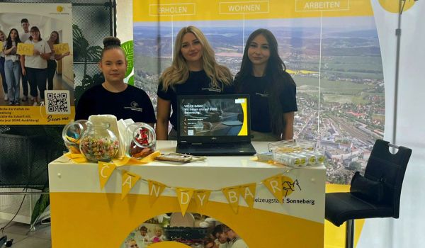 Drei Auszubildende stehen hinter einem Infostand.