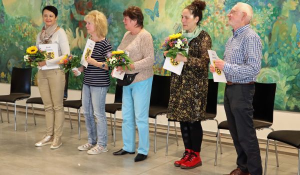 Fünf Personen stehen in einer Reihe nebeneinander. Sie halten eine Urkunde und Blumen in den Händen.