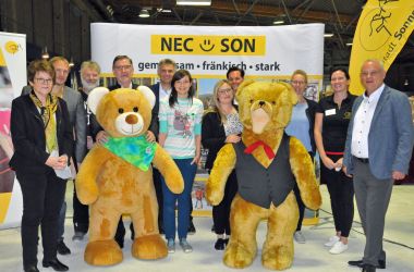 Mehrere Personen stehen mit zwei lebensgroßen Teddybären in einer Reihe.