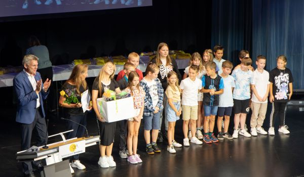 Kinder stehen auf einer Bühne. Links daneben steht der Bürgermeister und klatscht.