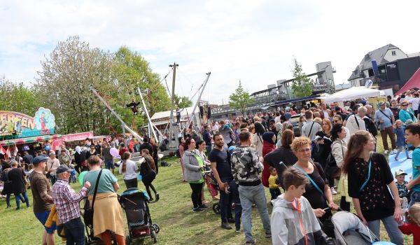 Viele Menschen auf einer Wiese. Im Hintergrund sind Fahrgeschäfte aufgebaut.