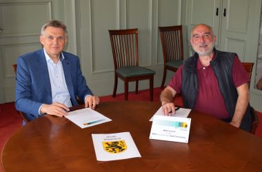 Zwei Männer sitzen an einem Tisch und unterschreiben eine Vereinbarung.