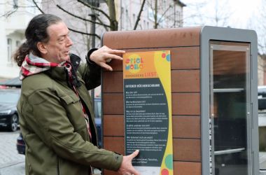 Ein Mitarbeiter montiert ein Schild an einem Bücherschrank.