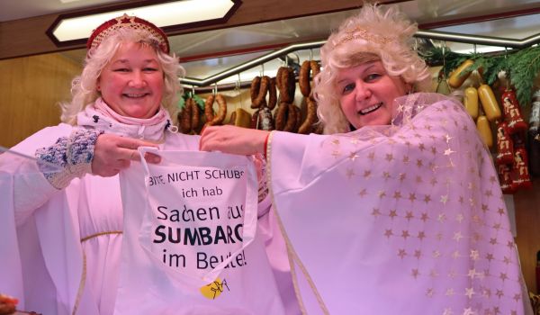 Zwei Frauen im Christkind-Kostüm halten einen Beutel hoch.