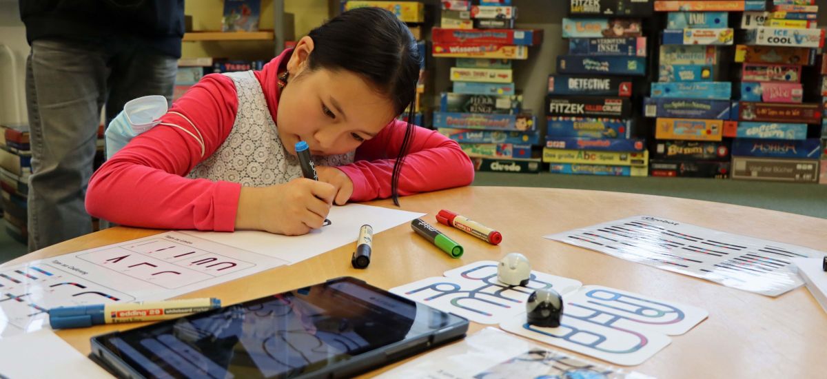 Ein Mädchen sitzt an einem Tisch und experimentiert mit einem Roboter.