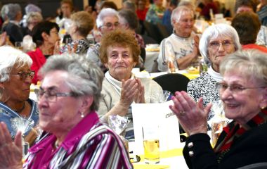 Senioren sitzen an Tischen und klatschen.