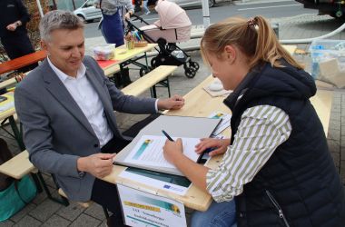 Der Bürgermeister Dr. Heiko Voigt und eine Frau sitzen an einem Tisch. Die Frau unterschreibt Unterlagen.