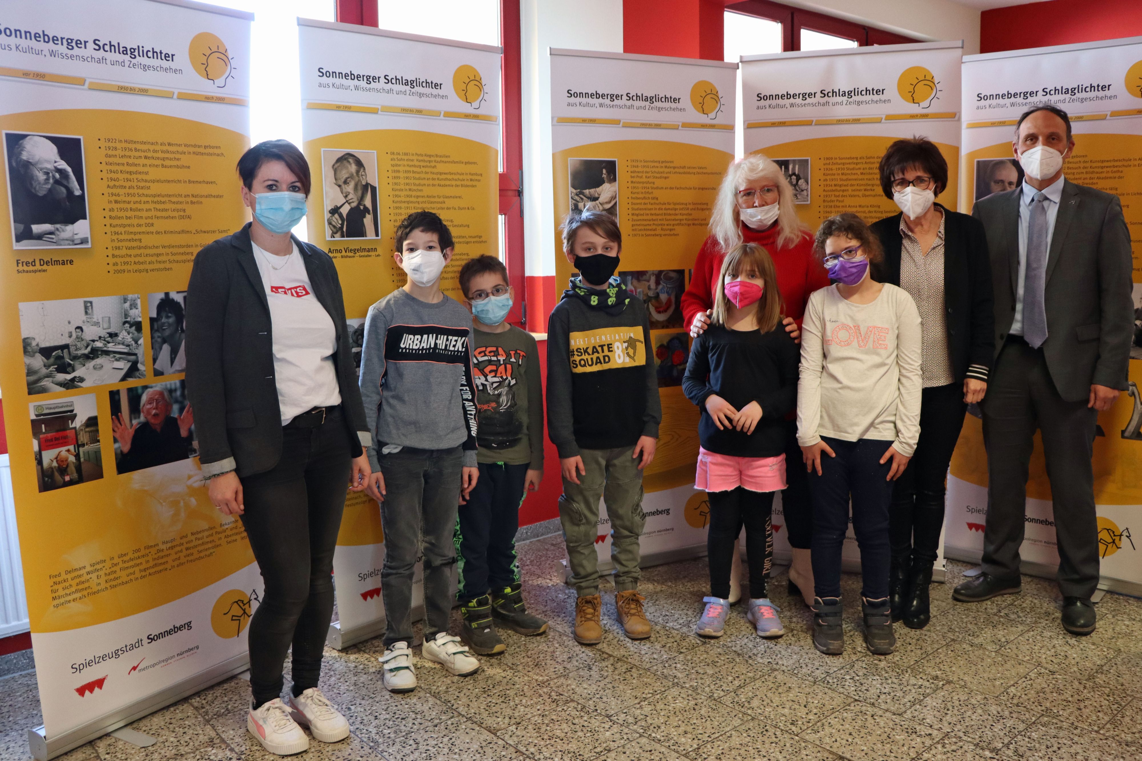 Eine Gruppe von Menschen steht vor veschiedenen Bannern in einer Schule.