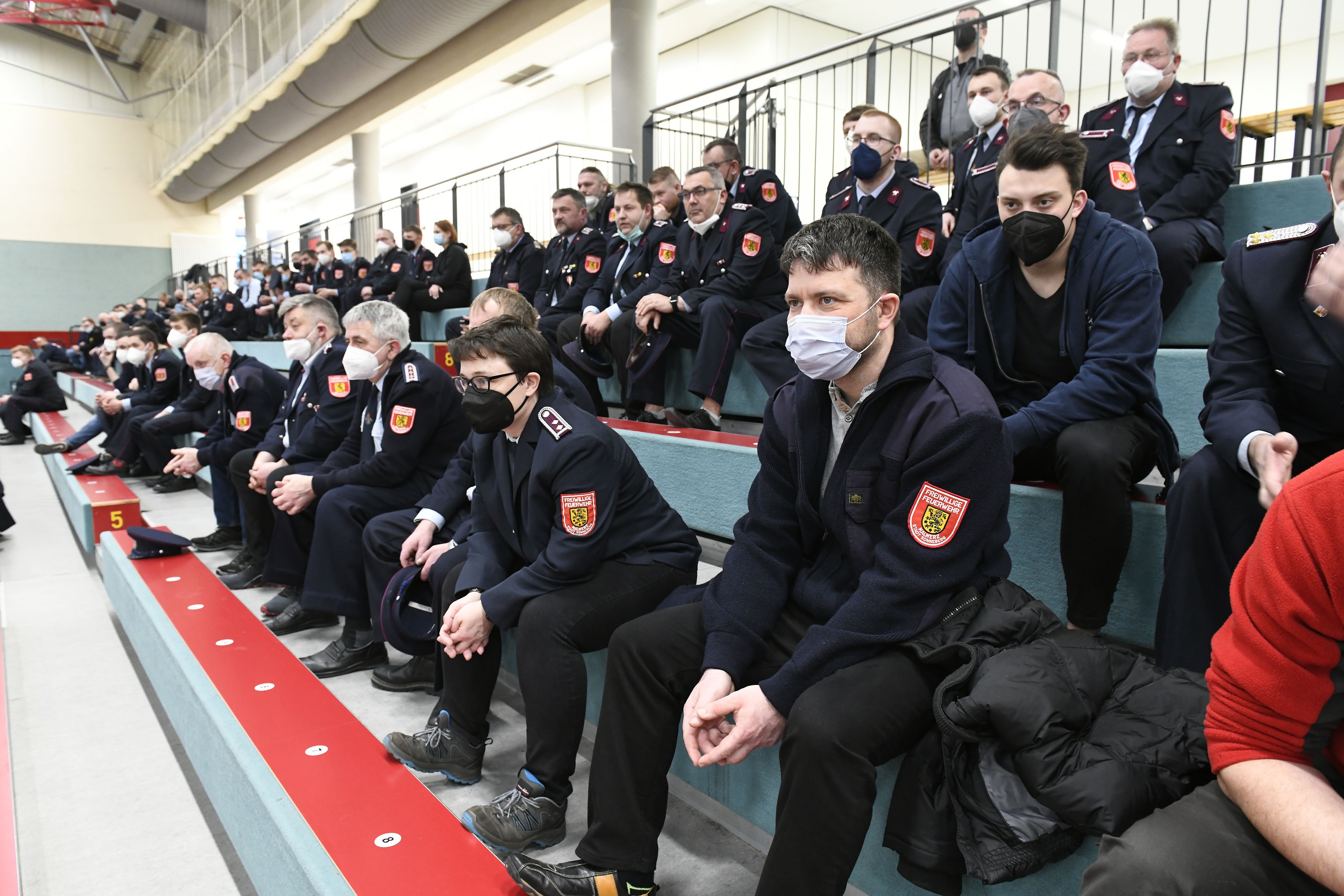 Eine Gruppe von Menschen in Feuerwehruniform sitzt auf einer Tribüne.