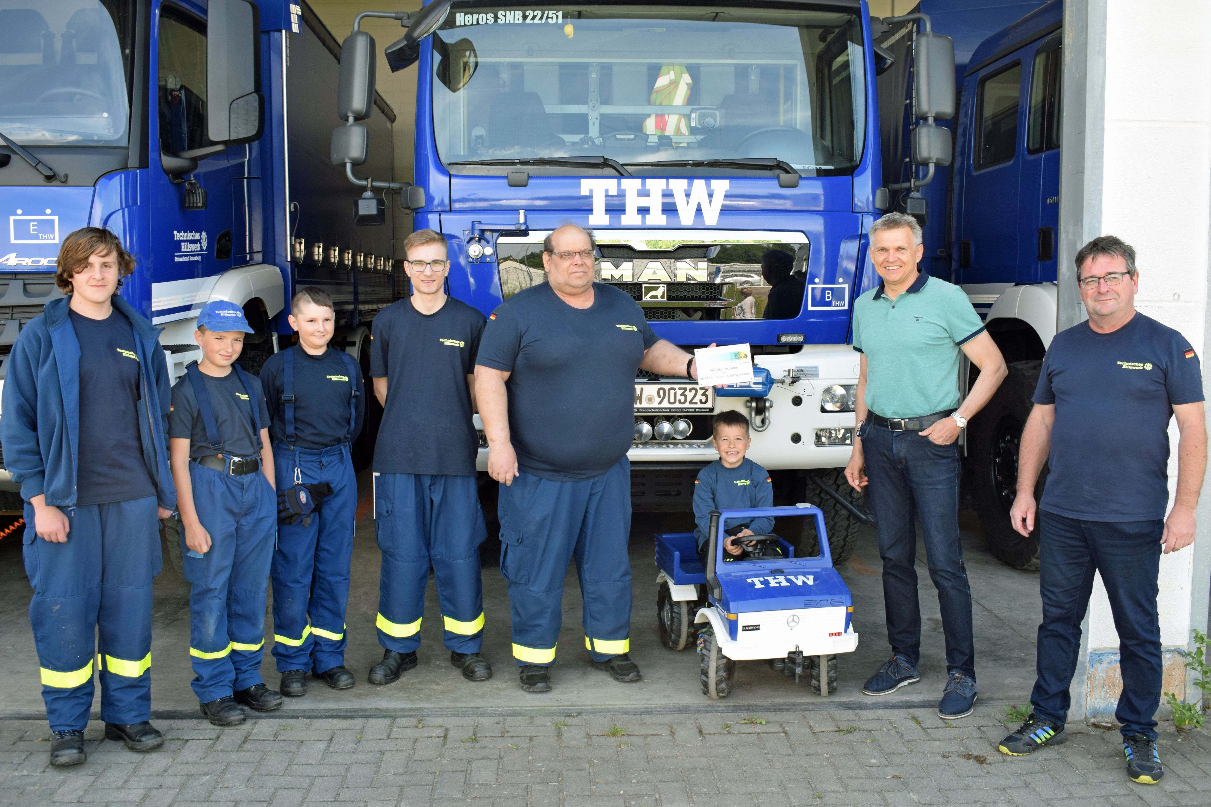 Mitglieder des Technischen Hilfswerks Sonneberg stehen mit dem Bürgermeister der Stadt Sonnebrg in einer Reihe. Im Hindergrund sind blaue THW-Einsatzfahrzeuge.