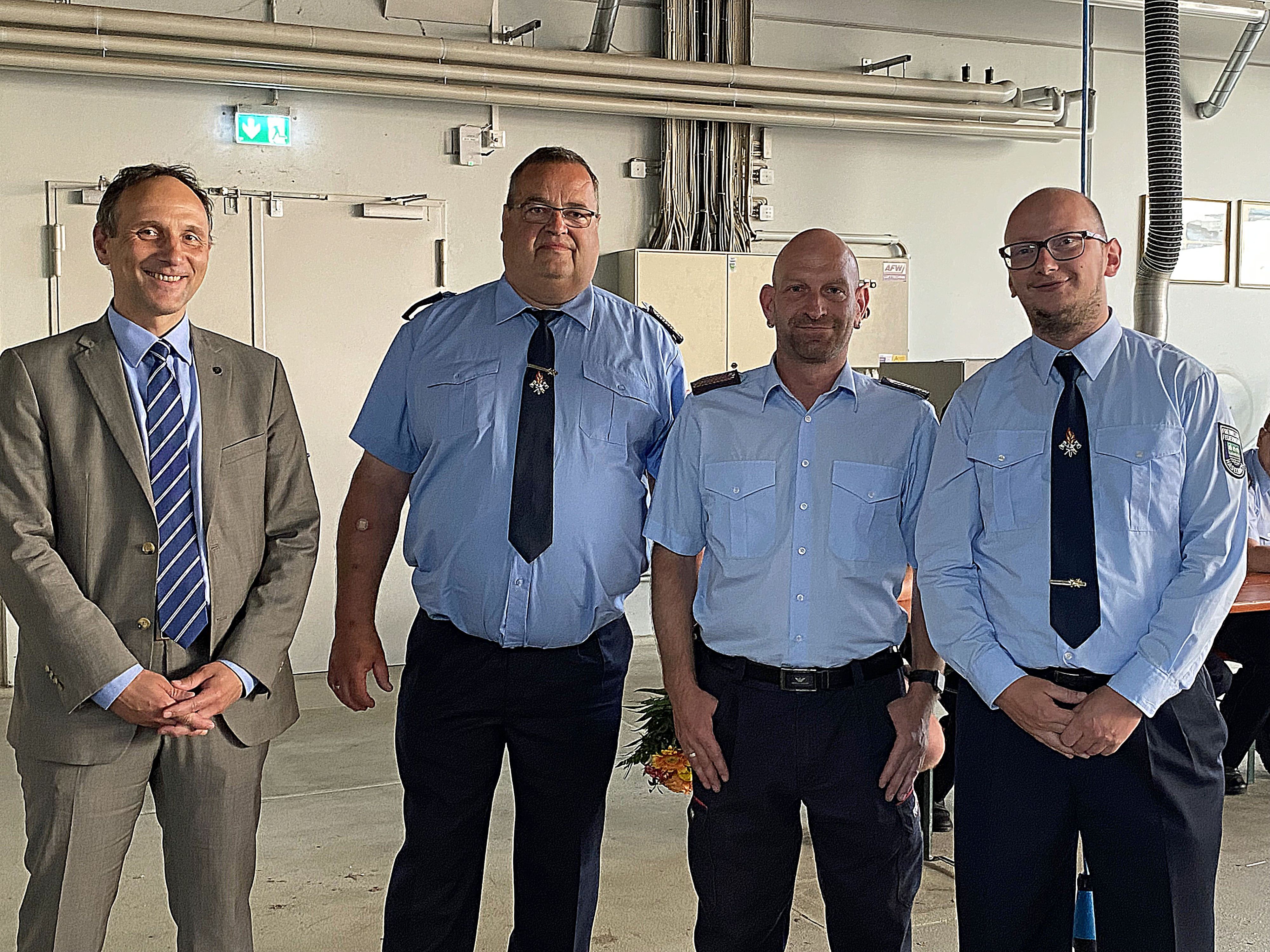 Drei Feuerwehrmänner in Uniform stehen nebeneinander. Links davon steht ein Mann im Anzug. Es ist der Hauptamtliche Beigeordnete Christian Dressel.