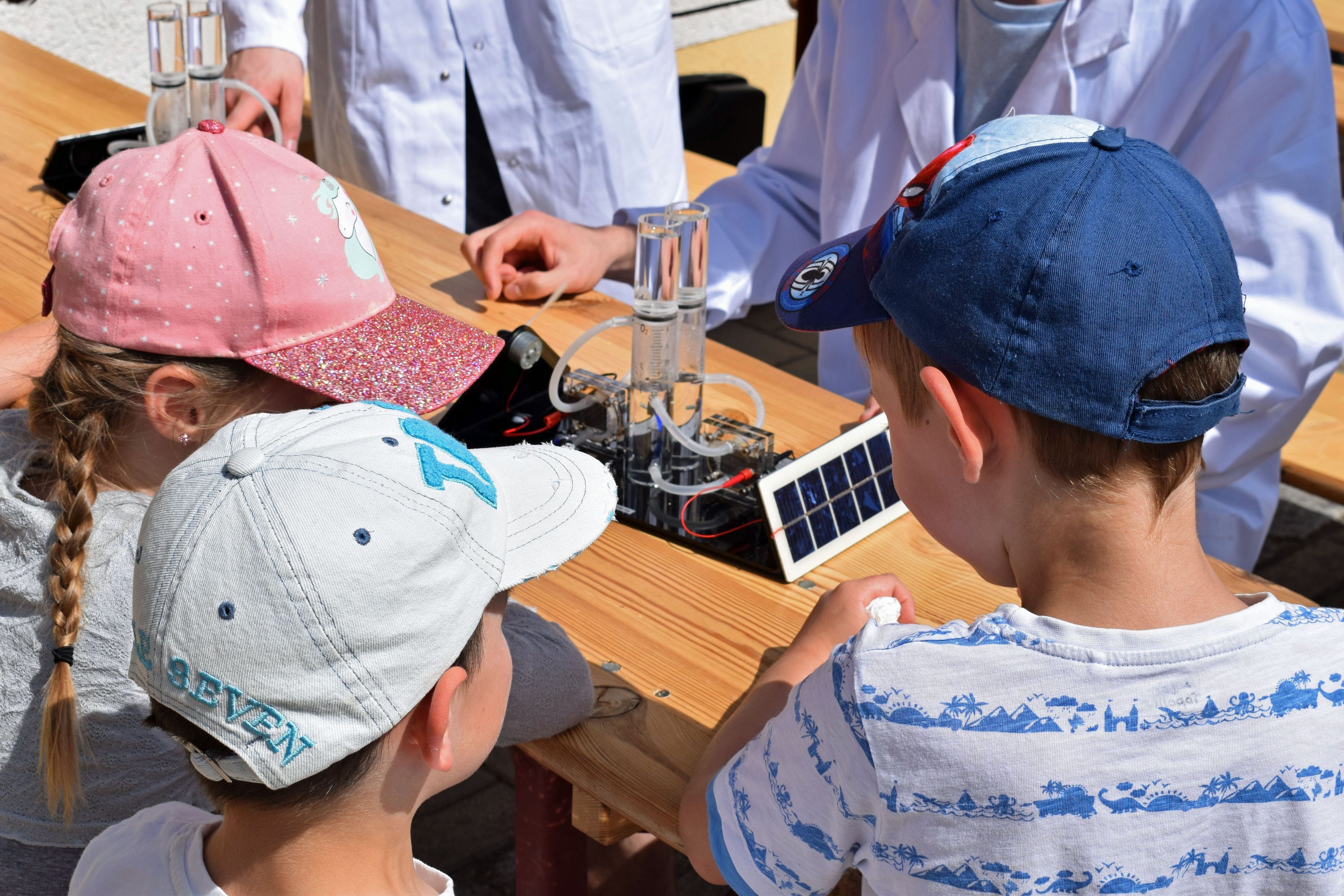 Drei Kinder stehen an einem Tisch. Auf dem Tisch steht eine Brennstoffzelle zum Experimentieren mit Wasserstoff.