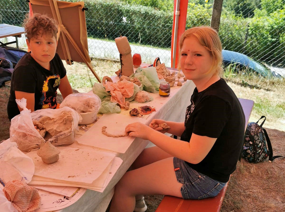 Zwei Kinder sitzen an einem Tischen und modellieren Figuren Ton.