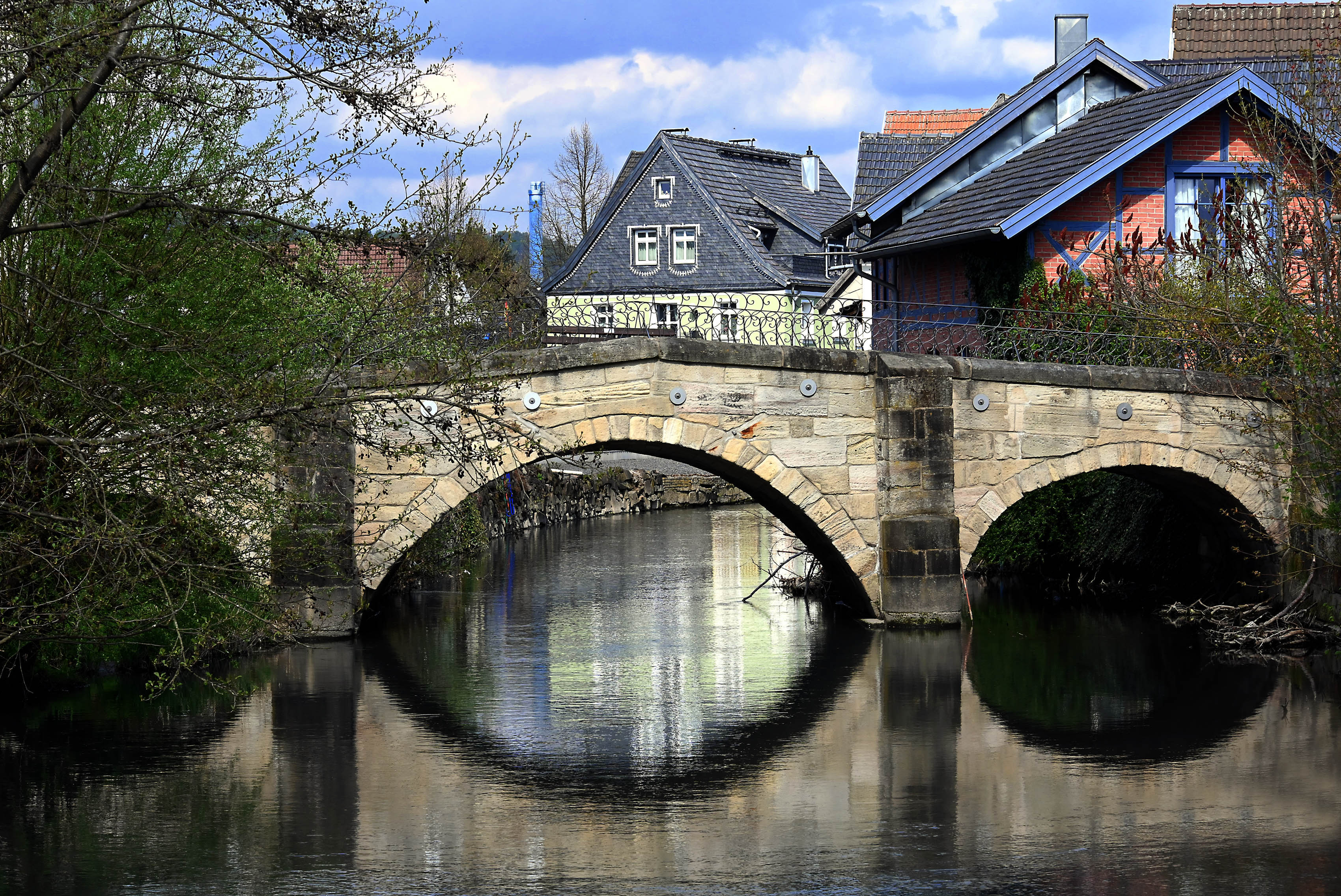 Eine Brücke aus hellem Sandstein die über einen Fluss führt. Im Hintergrund stehen Häuser.