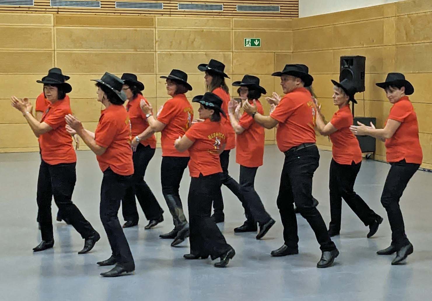 Personen mit roten T-Shirts und schwarzen Hüten Tanzen in einer Gruppe.